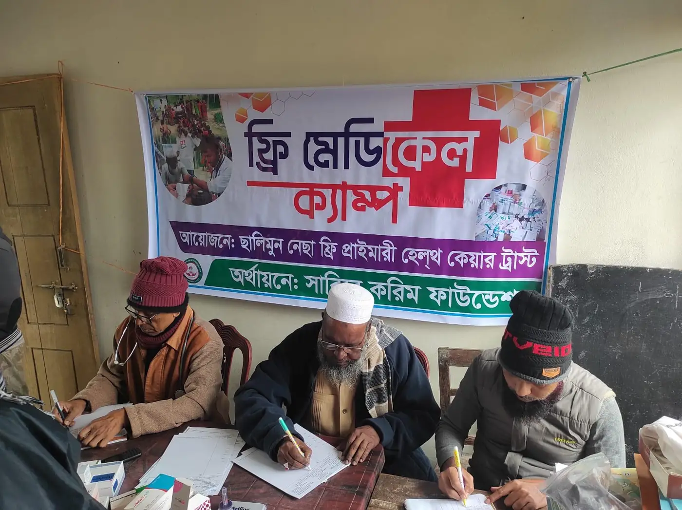 Doctors and volunteers at a free medical camp in Bangladesh, beneath a Bengali banner