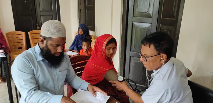 A doctor taking a woman&rsquo;s blood pressure while a volunteer takes notes